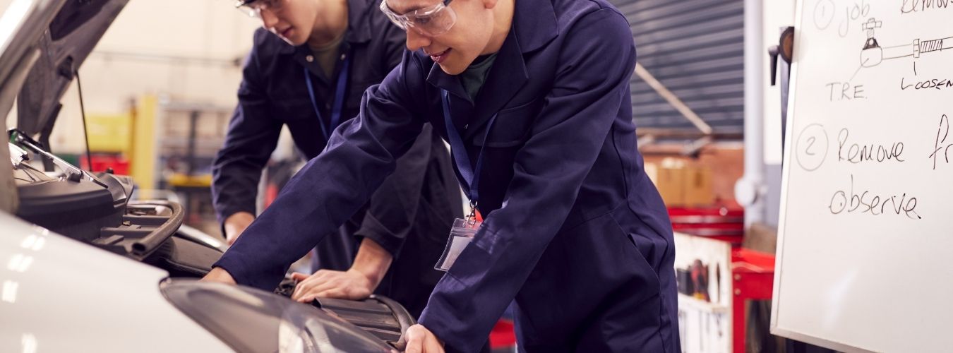 Two people in overalls looking at car engine in bonnet