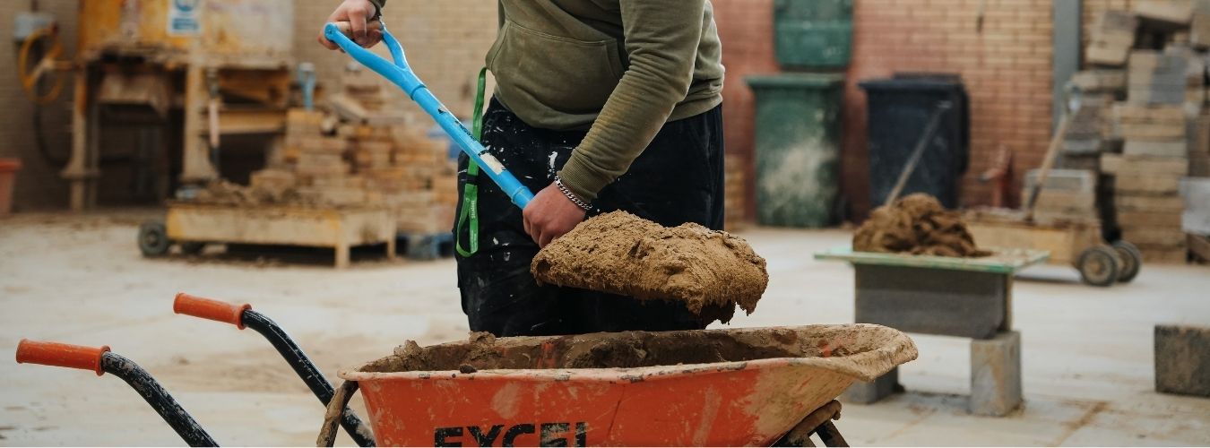 Person holding spade of cement over wheel barrow