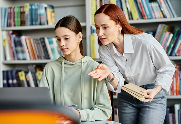 Student on laptop with teacher supporting 