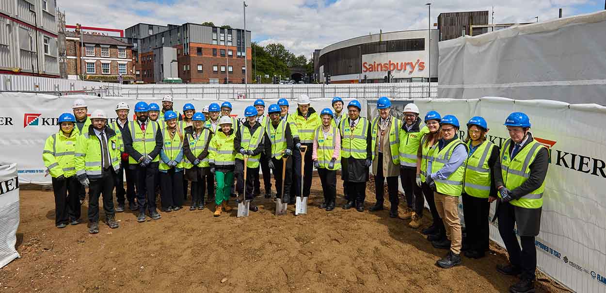 Group of people standing outside wearing PPE with some holding a spade digging into the ground.