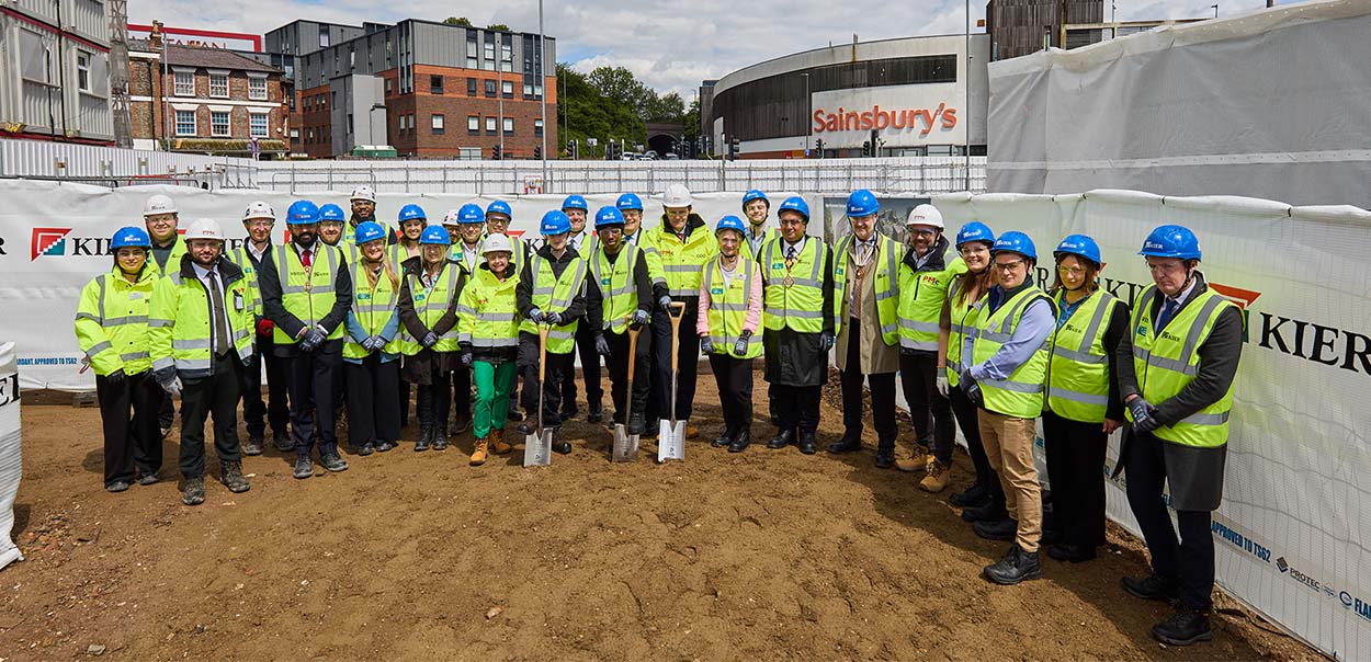 Group of people standing outside wearing PPE with some holding a spade digging into the ground.